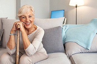 Woman in beige leaning on walking stick smiling