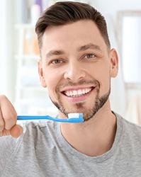 Man in grey shirt smiling and holding toothbrush