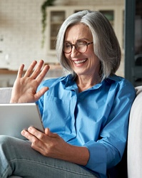 Older woman looking at tablet smiling with implant dentures in Boston