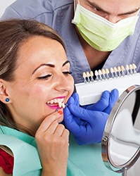 Woman at dentist’s office comparing shades for porcelain veneers in Boston