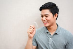 Man looking at an Invisalign retainer and smiling