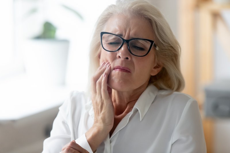 Woman with glasses on couch touching jaw