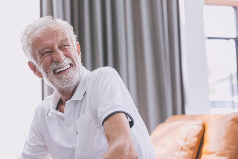 Man with new dentures sitting and smiling on couch