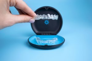 Fingers holding Invisalign in front of a blue background