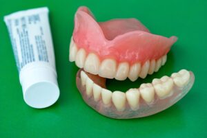 Dentures next to adhesive cream on a green background